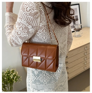 Petit sac matelassé marron à chaîne dorée porté par un mannequin dans un décor intérieur