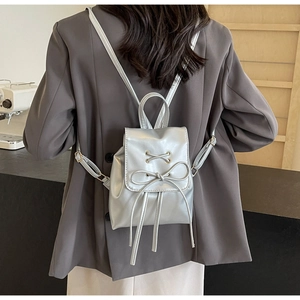Détail d'un mini sac à dos argenté avec nœud décoratif porté par un mannequin en veste