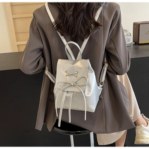 Silver mini bow backpack styled on a model with metallic eyelets and PU leather finish
