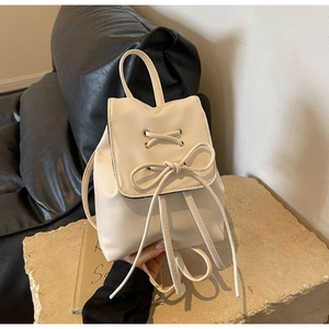 Detail view of cream PU leather backpack featuring metal eyelets and large bow decoration