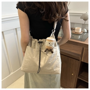 Detail of beige drawstring bucket bag featuring a cute plush coffee cup charm on the side