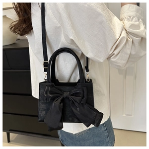 Model wearing a black shoulder bag with a large silk bow and gold hardware detail