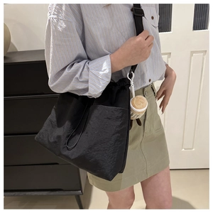 Detail view of black nylon shoulder bag featuring drawstring closure and plush pendant