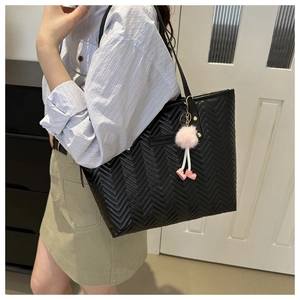 Dettaglio della borsa tote nera trapuntata a V con pompon rosa e targhetta moda