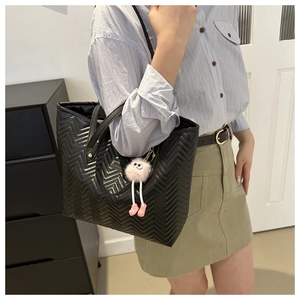Borsa tote nera trapuntata con ciondolo rosa mostrata dal modello in abbigliamento casual