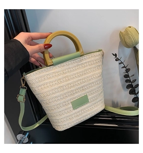 Detail of hand-woven straw bucket bag with resin handle and green leather accents