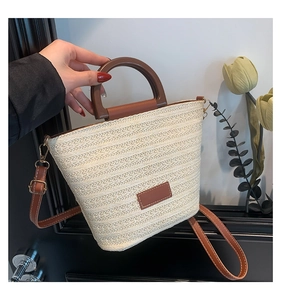 Detail of straw bucket bag showing wood ring handle and brown leather shoulder strap
