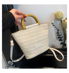 Detail of cream woven bucket bag featuring yellow circular handle and faux leather strap