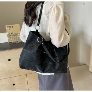 Detail of black tote bag with pleated texture and silver metal rings on model