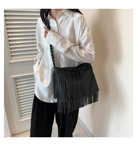 Detail view of the black fringe hobo bag with woven strap worn by a model in casual style