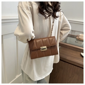 Detail of V-quilted texture and gold metal buckle on a brown leather crossbody bag