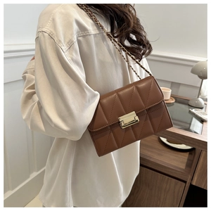 Detail of a brown quilted crossbody bag with a gold lock and leather chain strap