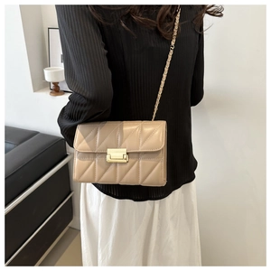 Detail of khaki quilted crossbody bag with gold rectangular clasp on model's outfit