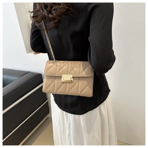 Detail of beige quilted shoulder bag featuring gold chain strap and metal clasp on model
