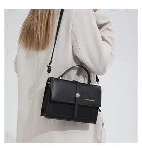 Détail d'un sac bandoulière noir minimaliste avec boucle dorée sur un blazer ivoire