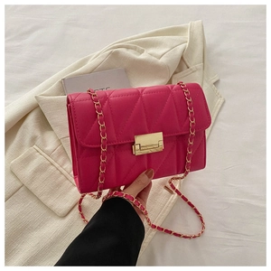 Detail of rose red quilted crossbody bag with gold buckle and chain on beige blazer