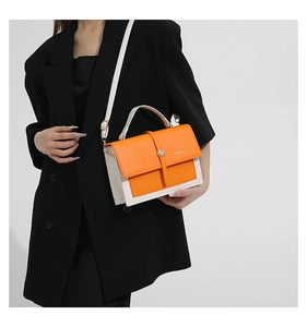 Détail du sac bandoulière orange et crème porté sur une veste de blazer noire chic