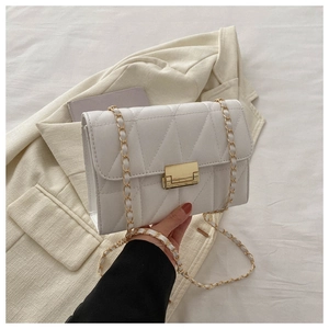 Detailed close-up of white quilted faux leather bag with gold lock and chain strap