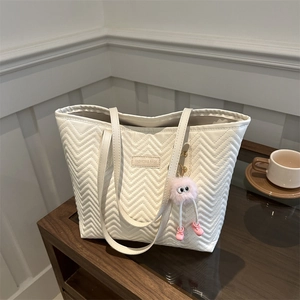 Large off-white quilted tote bag with chevron pattern and pink monster charm on wood surface