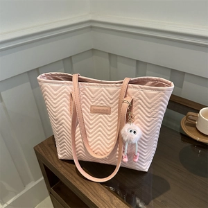Pink quilted tote bag with wave pattern and cute plush charm on a wooden surface
