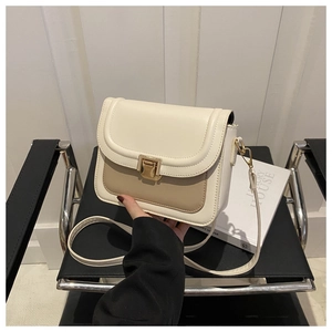 Détail d'un sac besace bicolore avec boucle en métal doré sur une chaise moderne