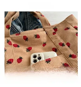 Detail shot of khaki corduroy tote bag with strawberry print and front phone pocket