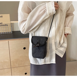 Detail of dark denim phone bag with horn buckle on model in minimalist setting