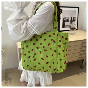 Detail of green corduroy tote bag with strawberry print worn by model in bright room