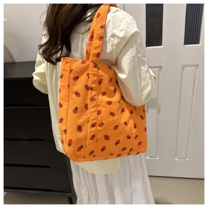 Detail of orange corduroy tote bag with strawberry embroidery worn by a model