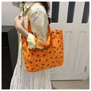 Detailed shot of an orange corduroy tote bag with red strawberry prints on a model