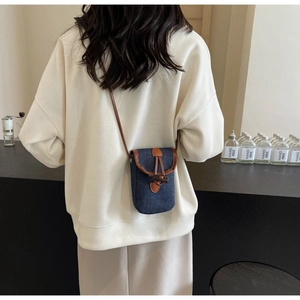 Detail of blue denim crossbody phone bag with brown leather trim and toggle closure