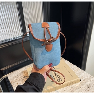 Close-up of light blue denim phone bag with brown leather trim and retro horn buckle