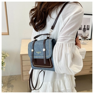 Detail of vintage denim and brown leather backpack with gold lettering on white lace shirt