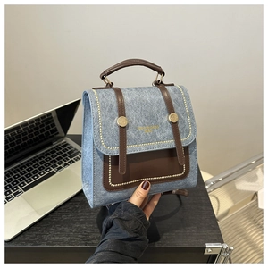 Detail of blue denim and brown leather handbag with gold bead trim and metal fasteners