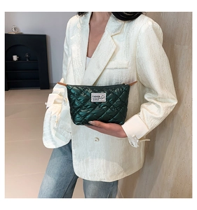 Gros plan sur une pochette matelassée vert foncé au fini satiné tenue par un mannequin