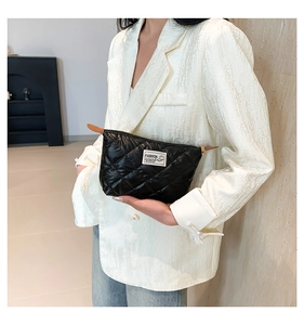 Détail d'une pochette en nylon matelassé noir avec écusson mode et fermeture éclair dorée