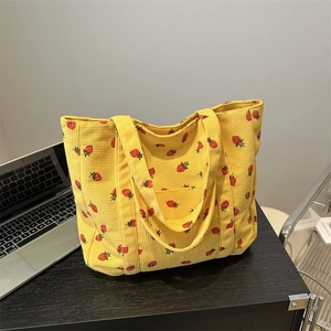 Yellow corduroy tote bag with red strawberry print on dark wood desk in casual setting