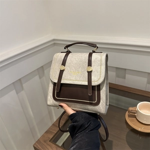 Vintage style beige and brown leather small backpack held in a minimalist indoor setting