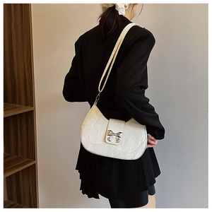 Detail of white bow shoulder bag with metallic clasp worn by model in black outfit