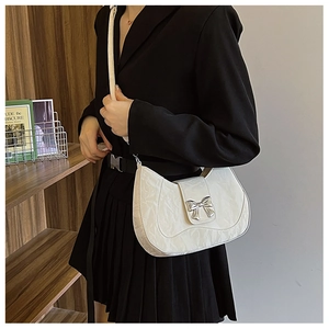 Detail of off-white pleated moon bag with silver bow buckle on model in black suit