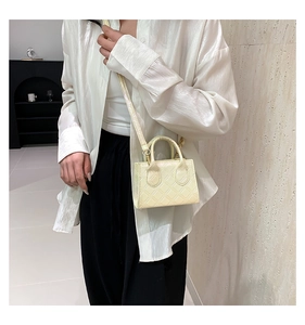 Detail of cream quilted crossbody bag with glossy finish and top handles on a model