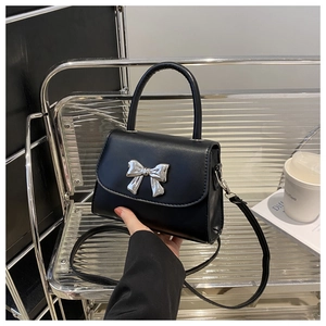 Detail of black crossbody bag with silver bow ornament on a minimalist shelf