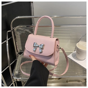 Close-up of pink crossbody bag with silver bow ornament on textured leather