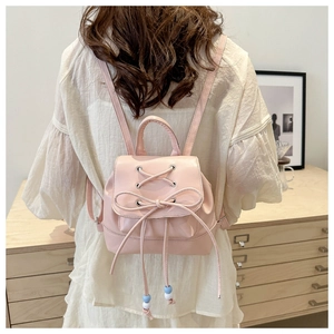 Rear view of a pink mini backpack with lace-up bow detail worn by a model in a soft dress