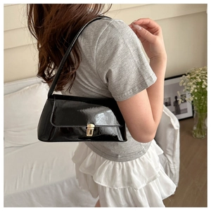 Close-up of black patent leather shoulder bag with a gold metal clasp shown on a model
