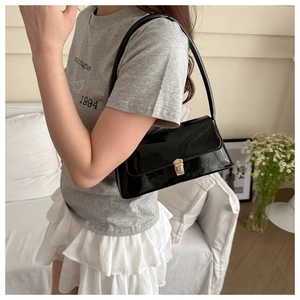 Close-up of black patent leather underarm bag featuring a metallic gold square buckle