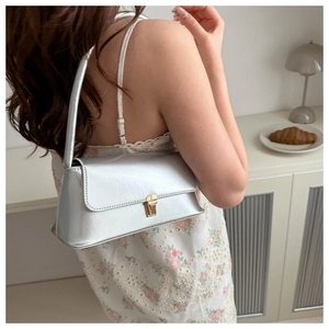 Detail of silver metallic shoulder bag with gold square buckle worn by a model