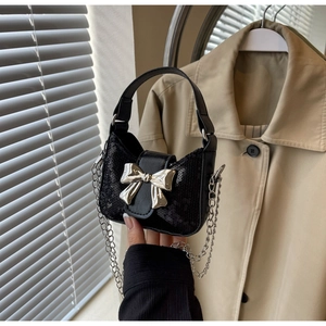 Détail du sac à paillettes noir avec un grand nœud métallique argenté et une chaîne