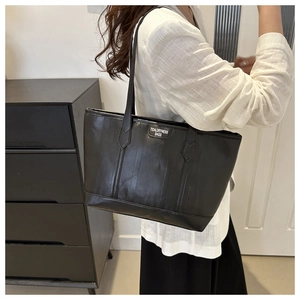 Vista laterale di una grande borsa tote in pelle nera con logo indossata da modella