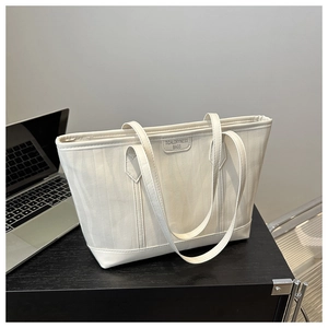 Dettaglio della borsa tote in tela beige con manici in pelle su una scrivania da ufficio
